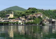 Un borgo sospeso nel tempo: acque cristalline, storia millenaria e una vista sul lago che lascia senza fiato Situato sulla sponda settentrionale del lago, il paese si erge su una rupe di lava leucitica a 173 metri sul livello del mare,